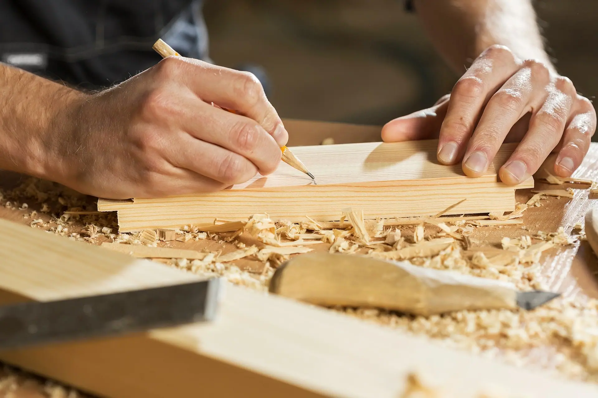 Carpenter’s hands marking a pine board with a pencil on a workbench covered in wood shavings